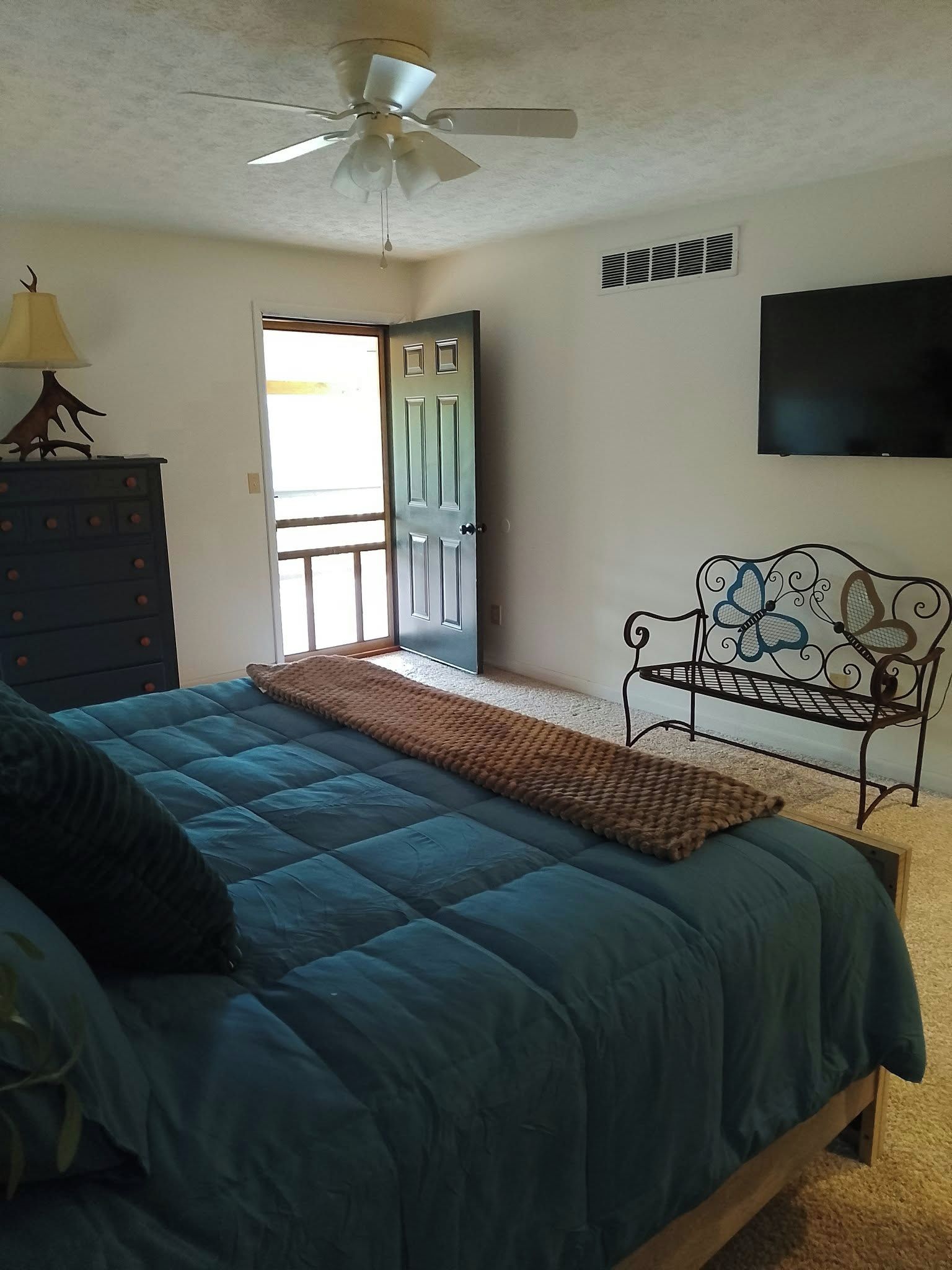A bedroom with a bed, a dresser, a bench, a ceiling fan, and a door.
