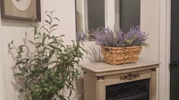 Une cheminée surmontée d’un panier tressé rempli de plants de lavande, un tableau encadré accroché au mur et une plante en pot placée à côté de la cheminée.