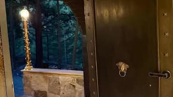 Una puerta de madera oscura con un picaporte de metal y cerradura, que da a un espacio al aire libre con un banco de piedra y un farol.