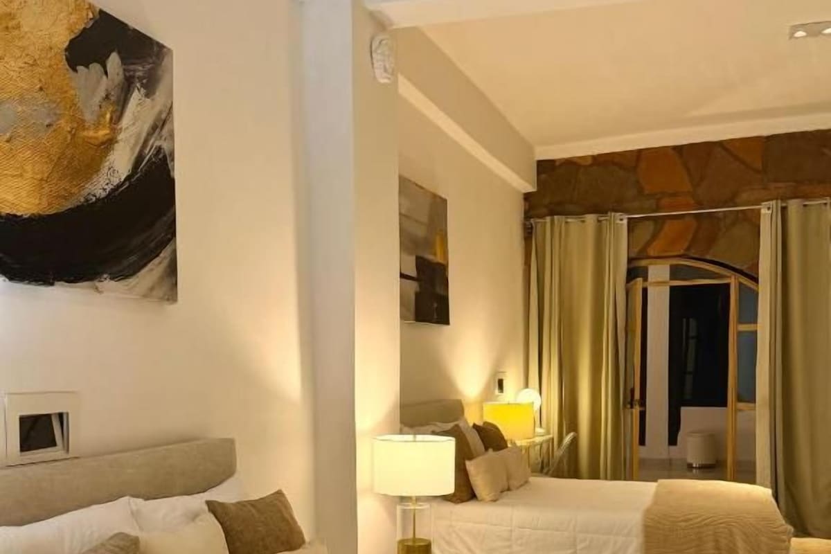 Quarto de hotel com uma cama grande, uma mesa de cabeceira com abajur e um quadro na parede.