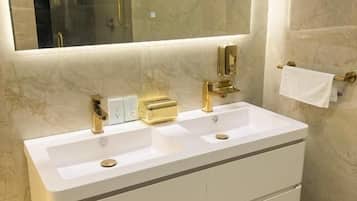 Un baño con tocador blanco, dos lavamanos, un espejo grande y un perchero para toallas.