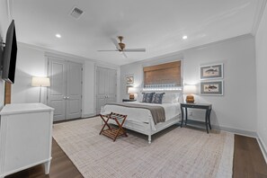 Ein Schlafzimmer mit Bett, Nachttischen, Deckenventilator und einem an der Wand befestigten Fernseher.