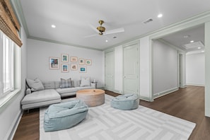 A modern living room with a sectional sofa, a round coffee table, and two bean bags. There are framed pictures on the wall and a ceiling fan. - Elegant Beachfront Retreat with Gorgeous Pool in Waveland, MS (Waveland)