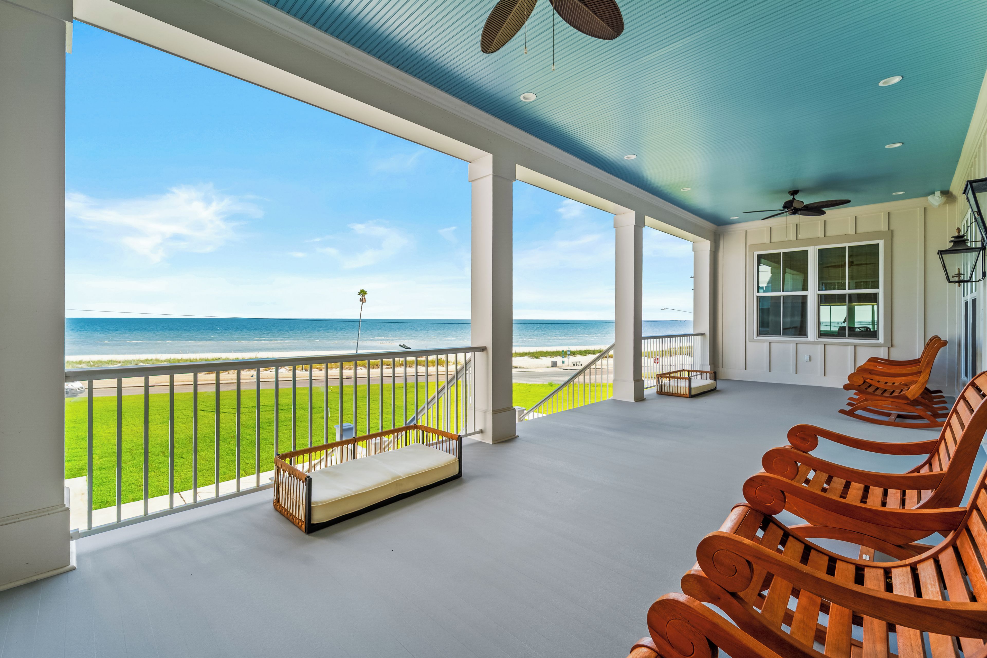 A spacious balcony with a view of the beach, wooden benches, and a ceiling fan.