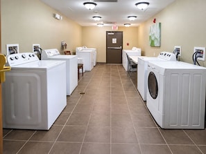 A laundry facility with multiple washing machines, a chair, and an exit door.