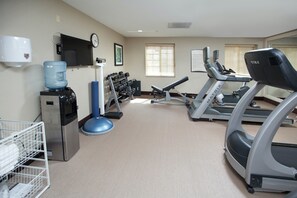 A gym with treadmills, weights, a water cooler, and a clock on the wall.