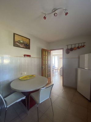 Una cocina con una mesa, sillas, un refrigerador y una puerta que da a otra habitación.