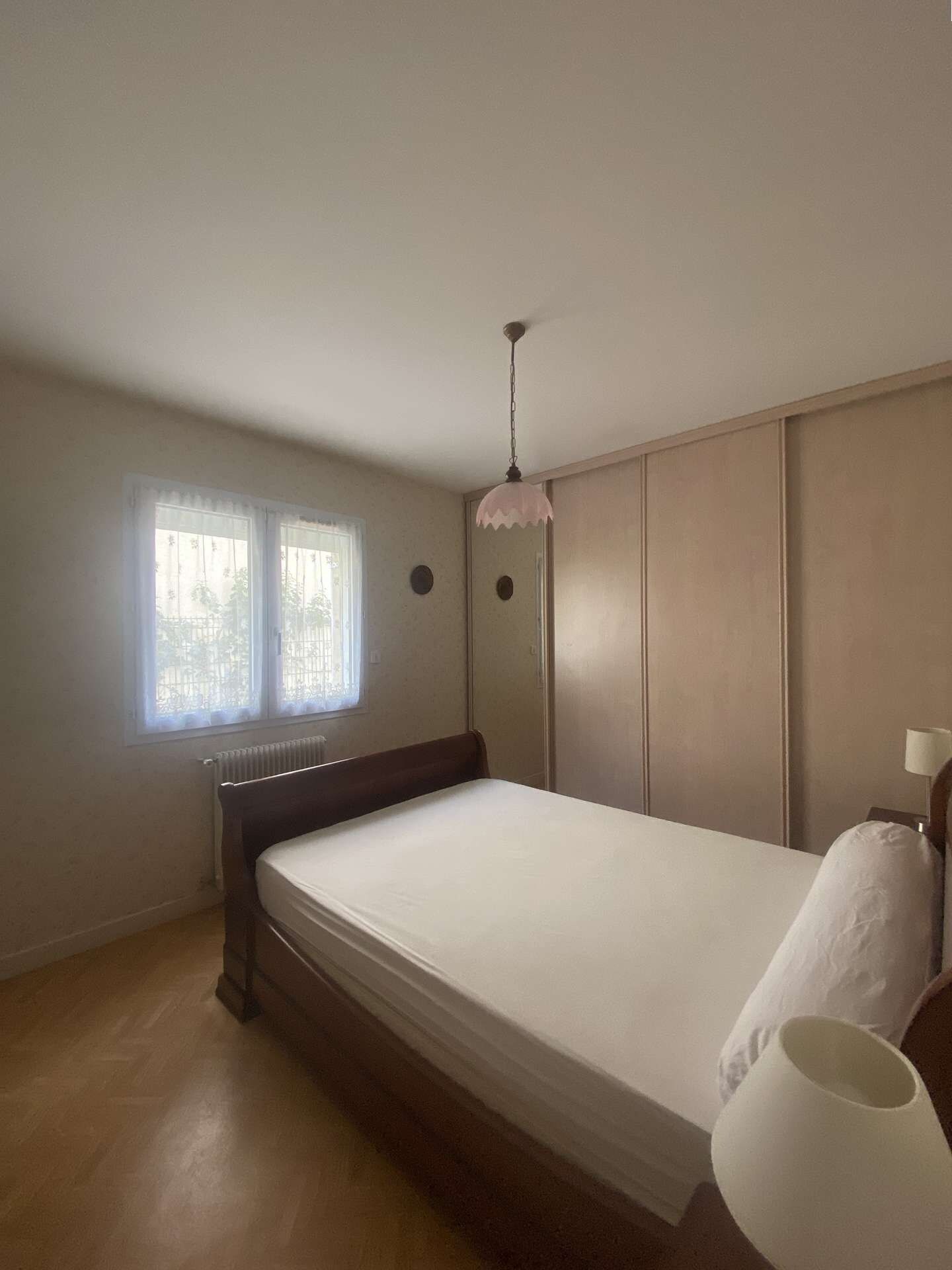 Une chambre avec un lit simple, une fenêtre avec des rideaux, un radiateur et un luminaire fixé au mur.