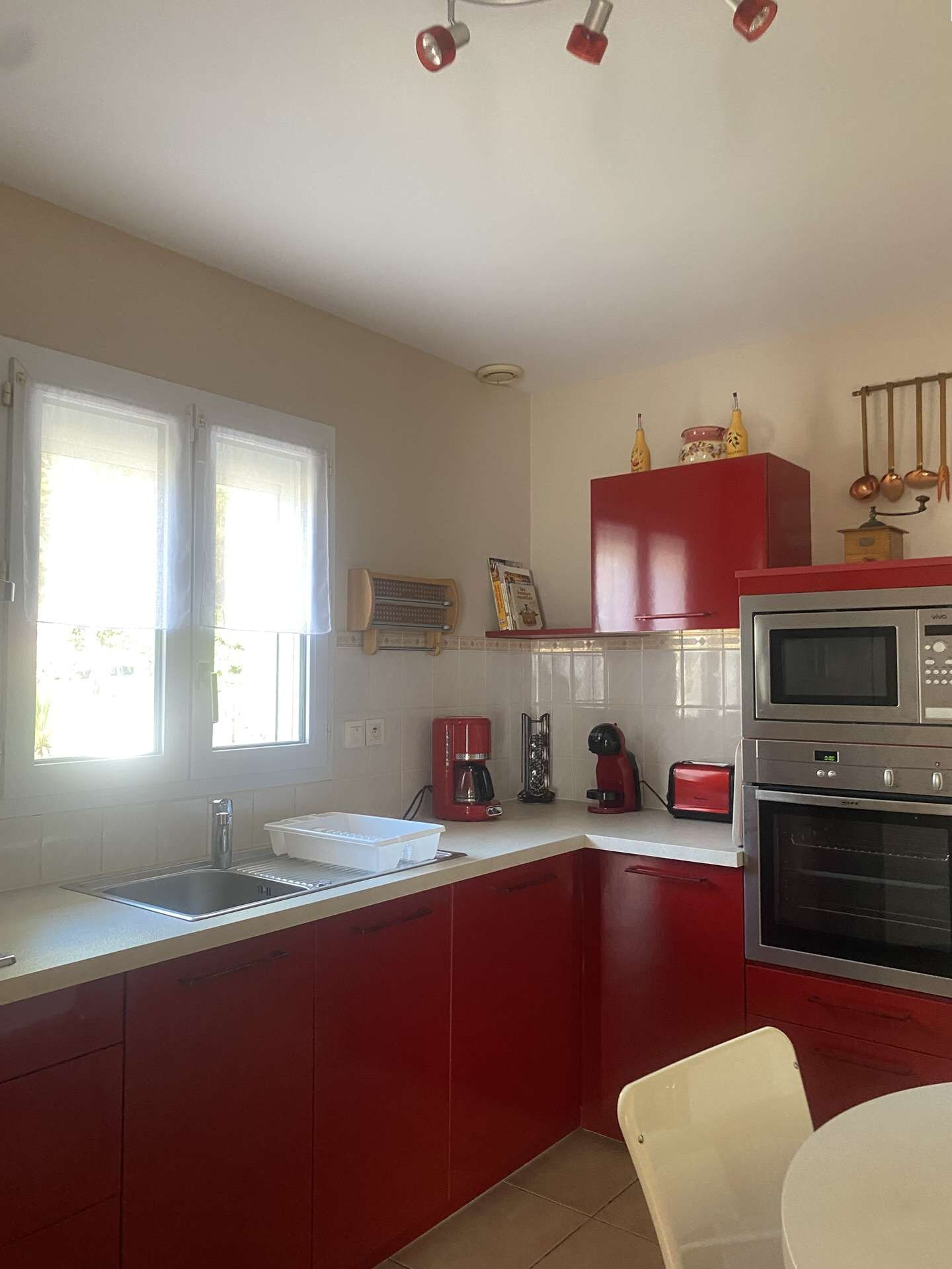 Een kleine keuken met rode kastjes, een magnetron, een broodrooster en een koffiezetapparaat.