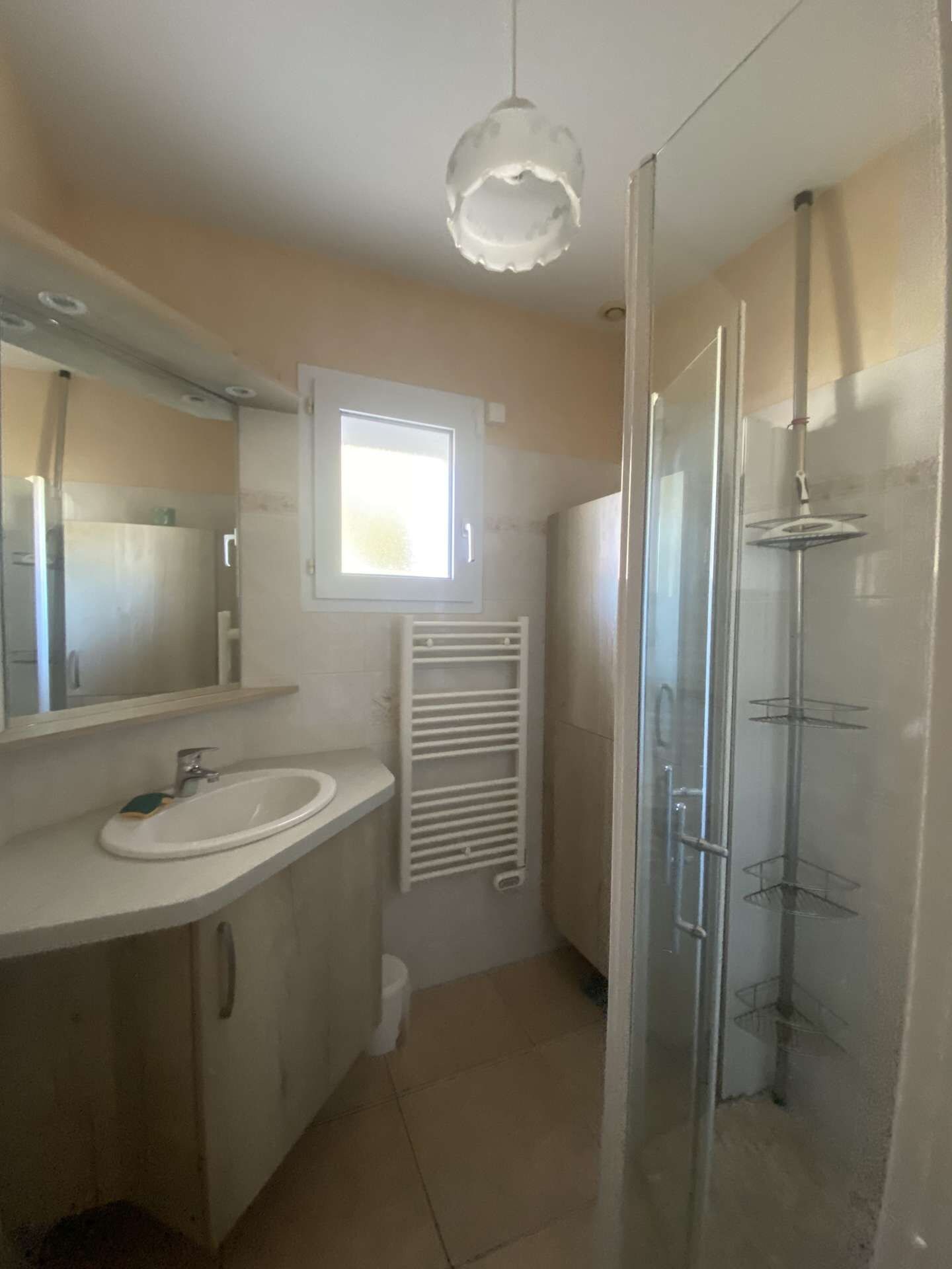 Un baño con lavamanos, espejo, ventana, ducha y toallero.