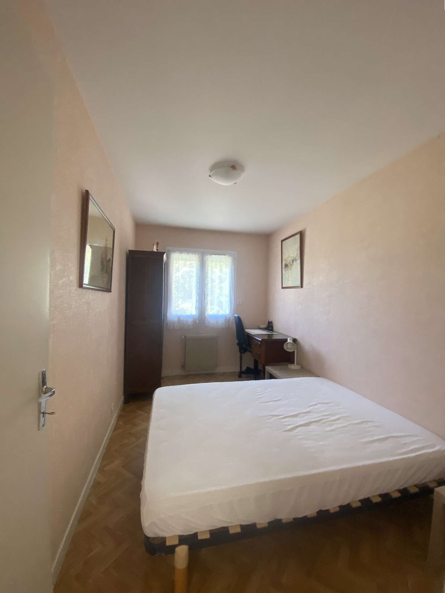 Een kamer met een bed, een bureau, een stoel, een kledingkast en een raam met gordijnen.