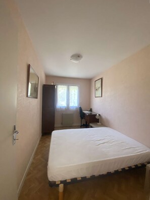 Una habitación con cama, escritorio, silla, armario y ventana con cortinas.