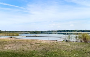 Ein ruhiger See mit einer anlegenden Plattform, umgeben von Wiesen und einem bewaldeten Ufer.