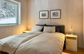 A bedroom with a bed, bedside tables, a window with a view of trees, and two framed pictures on the wall.
