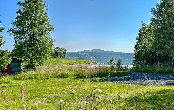 A rural landscape with a small shed, a gravel path, and a lake in the distance.
