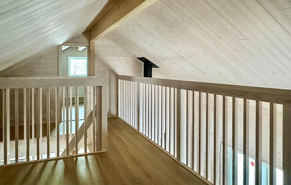 A high-ceilinged attic room with wooden beams, a sloped ceiling, and a view of a hallway.