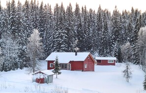 A red wooden cabin surrounded by a snowy forest.