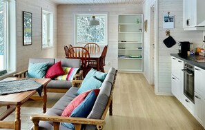 A cozy living room with a sofa, chairs, and a dining table. There is a kitchen area with cabinets and a stove.