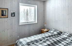 A bedroom with a bed, a nightstand, a lamp, and a window with a view of trees.