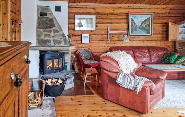 Interior acogedor de una cabaña con chimenea de piedra, sofá de cuero y paredes de madera.