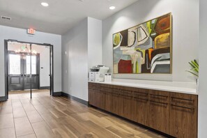 A hallway with a wooden floor, a reception desk with a large abstract painting, and an exit sign. - Endless Summer on the Warrior - Huntington Beach Meets Bama (Tuscaloosa)