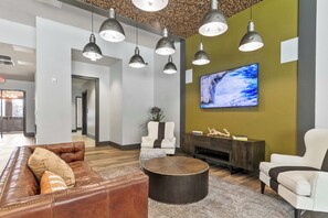 Eine moderne Lobby mit Ledersofas, einem runden Couchtisch, Pendelleuchten, einem Flachbildfernseher und einer Wanddekoration.