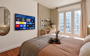 Ein Hotelzimmer mit Bett, Schreibtisch, Fernseher mit Streaming-Angeboten und einem Fenster mit Blick auf die Stadt.
