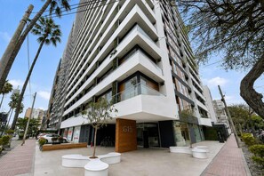 A modern multi-story building with a prominent entrance, large windows, and a landscaped area with planters. - Loft con vista al mar y piscina Barranco (Barranco)