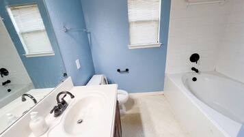 A bathroom with a white bathtub, a double sink, and a toilet.