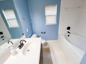 A bathroom with a white bathtub, a double sink, and a toilet. - Cosytastic Barn Ridge (Houston)