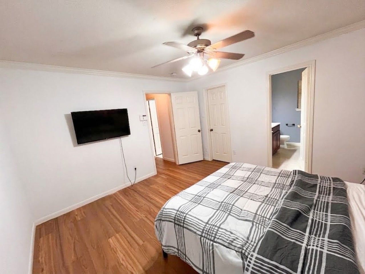 Ein Schlafzimmer mit einem Bett, einem Deckenventilator, einem Fernseher und einer Tür zu einem Badezimmer.