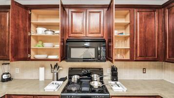 A kitchen with wooden cabinets, a stove, a microwave, and a blender.