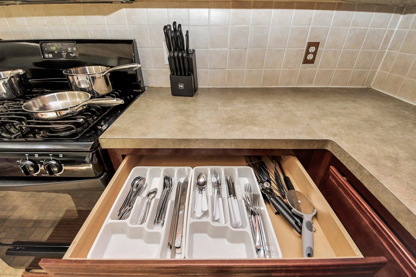 A kitchen with a stove, a drawer with utensils, and a knife block on the countertop.