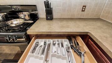 A kitchen with a stove, a drawer with utensils, and a knife block on the countertop.