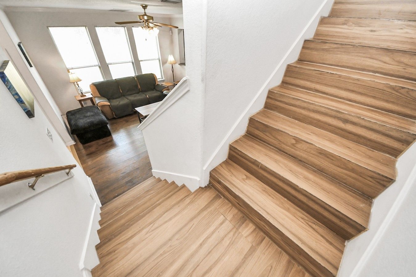 A wooden staircase with a handrail, leading to a room with a sofa and a lamp.