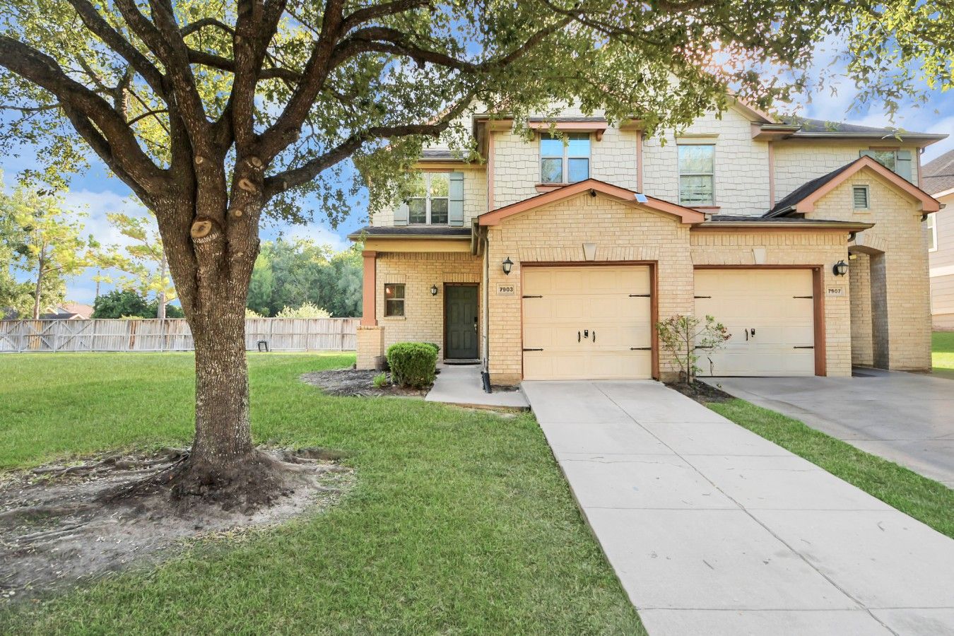 A two-story house with a front garage, a well-maintained lawn, and a large tree in the front yard.
