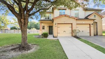 A two-story house with a front garage, a well-maintained lawn, and a large tree in the front yard.