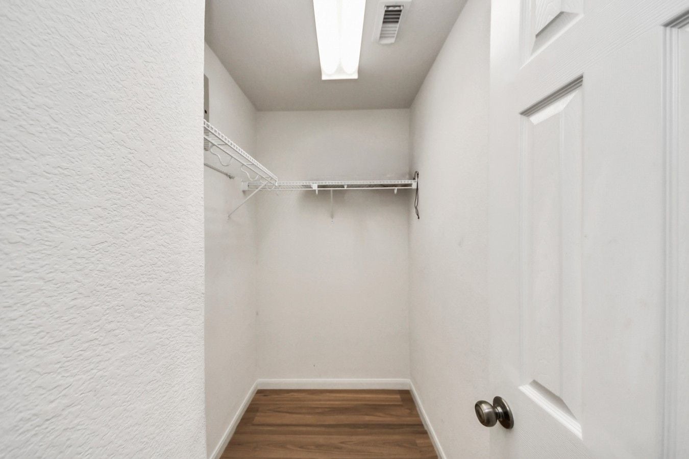 A narrow hallway with white walls, a wooden floor, a white door, and a metal rack on the wall.