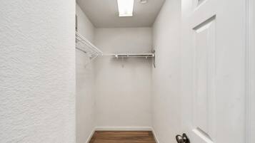 A narrow hallway with white walls, a wooden floor, a white door, and a metal rack on the wall.