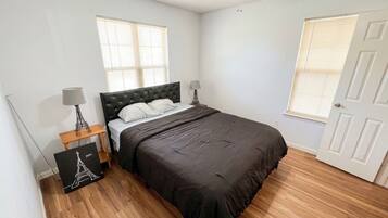 A bedroom with a bed, a ceiling fan, a nightstand with a lamp, and a picture frame.