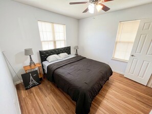A bedroom with a bed, a ceiling fan, a nightstand with a lamp, and a picture frame. - Cosytastic Barn Ridge (Houston)