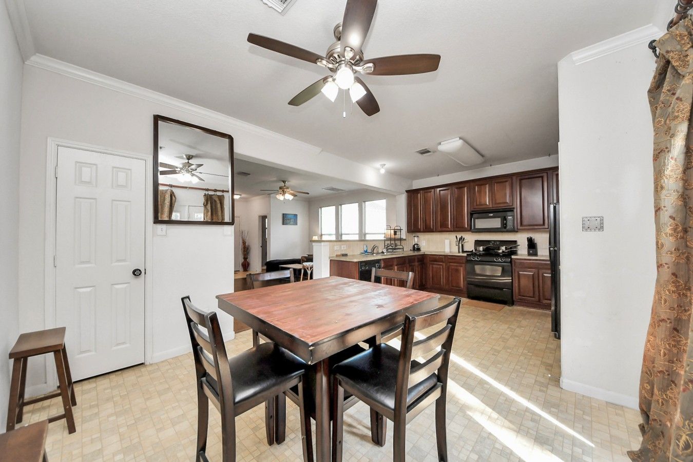 A dining area with a wooden table and chairs, a ceiling fan, and a kitchen in the background.