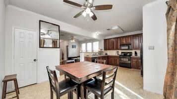 A dining area with a wooden table and chairs, a ceiling fan, and a kitchen in the background.