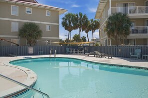 A swimming pool with lounge chairs and a table, surrounded by a fence and palm trees. - Sunset Harbor 322 | Sound & Pool Getaway (Navarre)