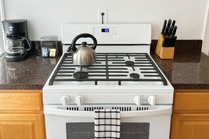 A kitchen with a white stove, a kettle, a coffee maker, and a knife block. - 2BR Steps from Wrigley Field (Chicago)