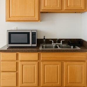 A kitchen with wooden cabinets, a stainless steel microwave, and a double sink. - 2BR Steps from Wrigley Field (Chicago)