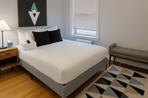 Een keurig opgemaakt slaapkamer met een bed, nachtkastje, lamp en een vloerkleed met een geometrisch patroon.