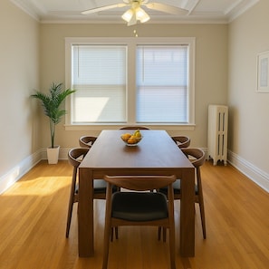 A dining area with a wooden table, four chairs, a bowl of fruit, a potted plant, and a radiator. - Feel at Home in our 2BR Apt (Chicago)