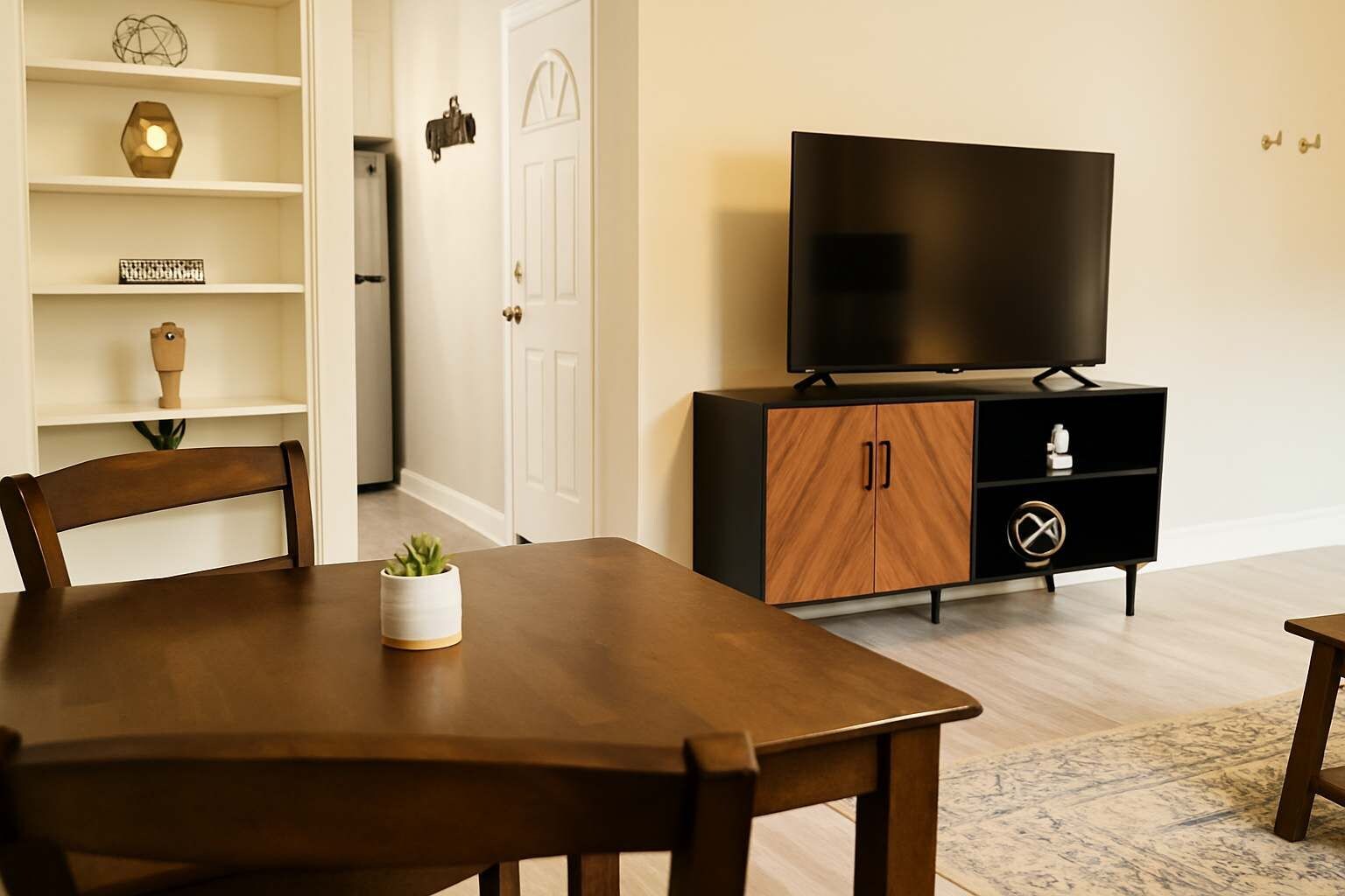 A modern living room with a wooden dining table, a TV on a black cabinet, and a white door.