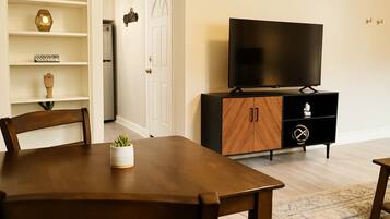 A modern living room with a wooden dining table, a TV on a black cabinet, and a white door.